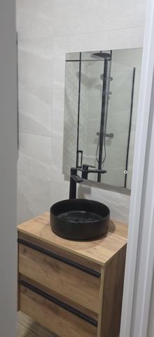 Lavabo sobre encimera. Mueble de dos cajones en acabado madera, con lavabo redondo negro y grifo alto.